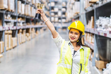 Happy woman warehouse worker holding a trophy after being selected as an outstanding employeeの写真素材