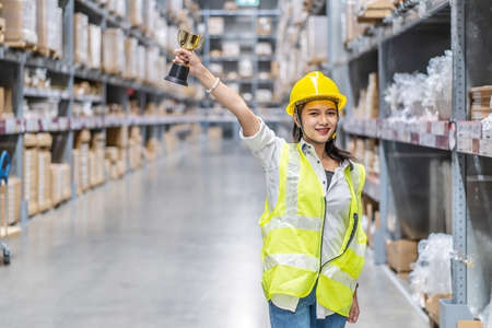 Happy woman warehouse worker holding a trophy after being selected as an outstanding employeeの写真素材