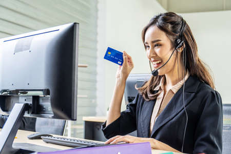Internet banking, online shopping and technology concept, happy smiling asian woman helpline operator showing credit card at officeの写真素材