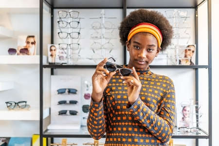 Need a new glasses.Young woman african american afro hair posing with new  glasses standing at in optical shop. modern ophthalmologist conceptの写真素材