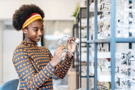 Need a new glasses. Young woman african american in optic store choosing a new eyeglasses frame. Medical, health care concept, used correct or assist defective eyesightの写真素材