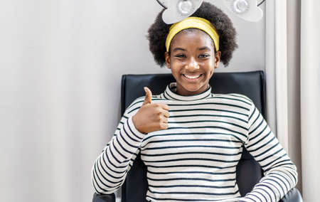 Smiling young woman african american afro hair show Thumbs up after doing eyesight measurement with optical phoropterの写真素材