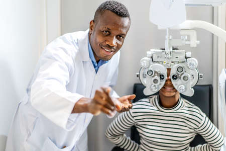 Optician doing optometry eye exam for black african american teen girl patient. Male optometrist...