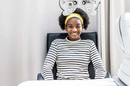 Smiling young woman african american afro hair after doing eyesight measurement with optical...