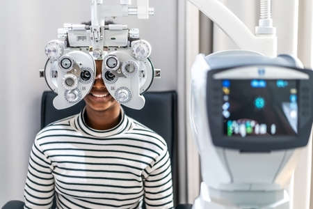 Smiling young woman african american afro hair doing Eye test on optical phoropter, checking on her...