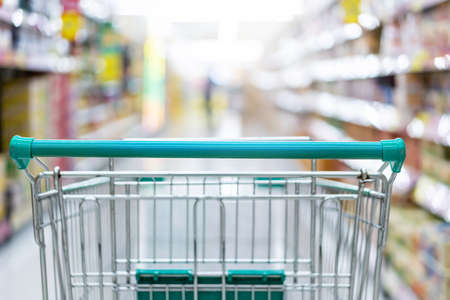 shopping cart in supermarket aisle with product shelves interior defocused blur backgroundの写真素材