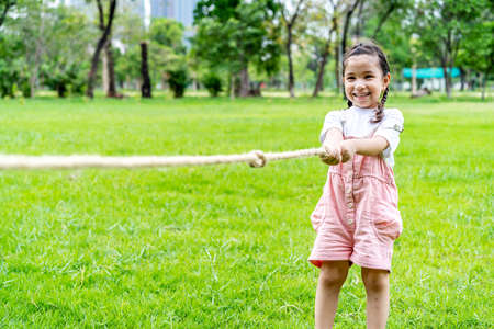 Cheerful child girl having fun to playing tug of war at the park, smiling girl pulling a rope on the green lawn, children sport concepの写真素材