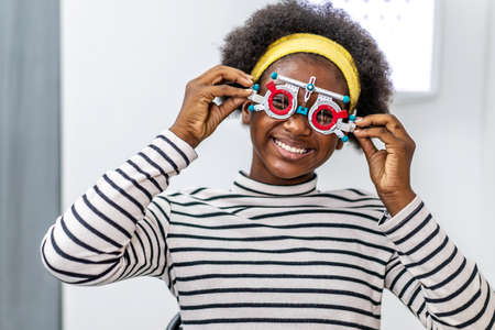 Smiling young woman african american checking vision with eye test glasses during a medical examination at the ophthalmological office, Checking eye vision by optician health examination conceptの写真素材
