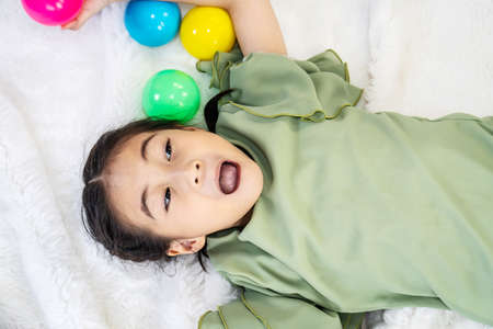 Asian little daughter is laughing and playing toy ball on white bed with feeling happy and cheerfulの写真素材