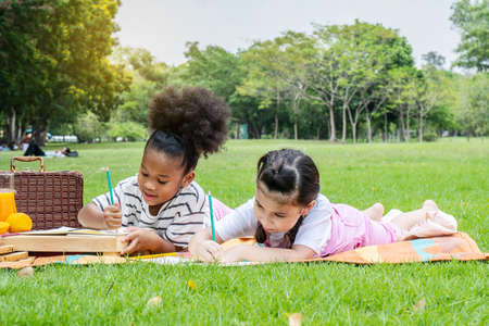 Two american african little girl lying and drawing with colored pencils at summer park, feel happiness, outdoor education conceptsの写真素材