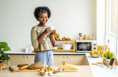 Young happy woman african american afro hair drinking coffee on the kitchen in the morning.の写真素材