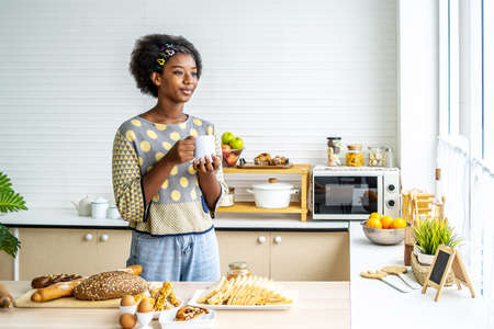 Young happy woman african american afro hair drinking coffee on the kitchen in the morning.の写真素材