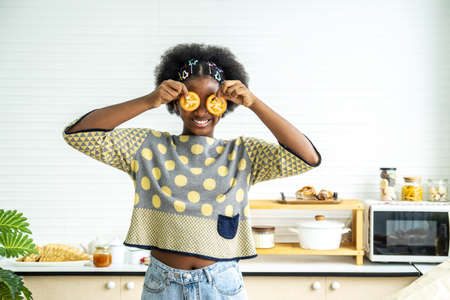 African american happy girl having fun with food vegetables at kitchen holds tomatoes before his eyes like in glasses, Teaching child to healthy and varied vegitarian foodの写真素材