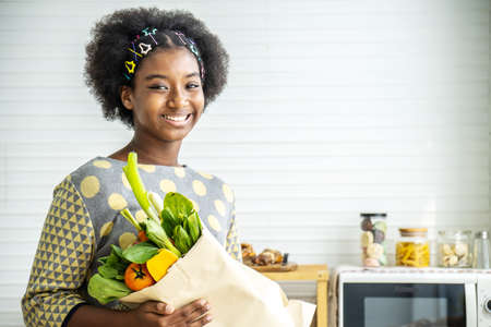 Happy healthy African american girl in the kitchen, Adorable girl smiling and holding paper bag with fresh food full of vegetables, Healthy eatingの写真素材