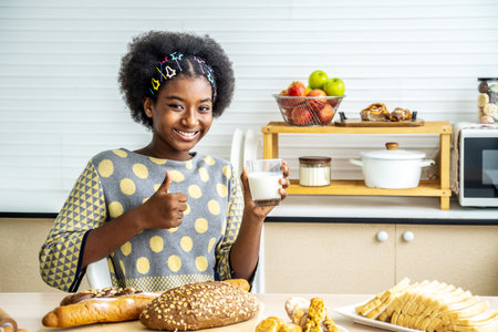 Young happy woman african american afro hair drinking a glass of milk at home happy with big smile doing ok sign, thumb up with fingers, excellent signの写真素材
