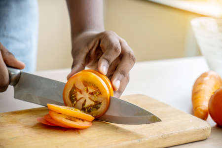Close up of hand african american girl chopping  tomatoes on cutting board with knife in kitchenの写真素材