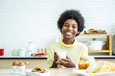 Child having breakfast. Happy cute African-American boy drinking milk and eating bread with egg. Kids eat on sunny morning. Healthy balanced nutrition for young kids.の写真素材