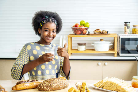 Young happy woman african american afro hair drinking a glass of milk at home happy with big smile doing ok sign, thumb up with fingers, excellent signの写真素材