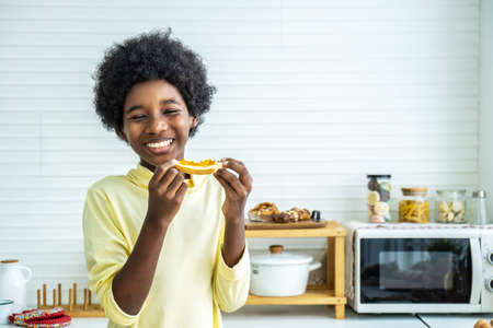 Adorable happy cute little boy eating toast with sweet jam for breakfast in kitchen at home in the morningの写真素材