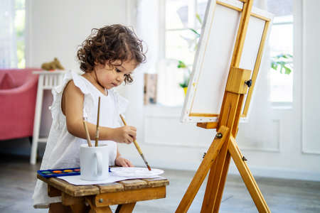 A little cute girl artist uses an acrylic paint brush to make her drawings on canvasの写真素材