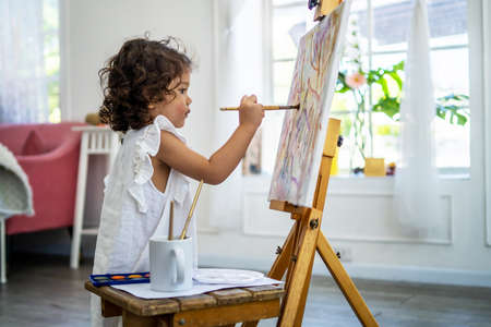 A little cute girl artist painting picture on canvas with watercolor paints at homeの写真素材