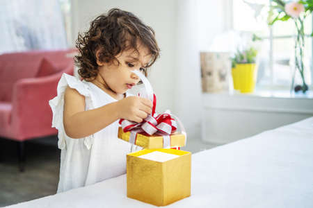 Portrait of adorable little girl opening birthday box gift and looking inside with surprised joyful facial expressionの写真素材