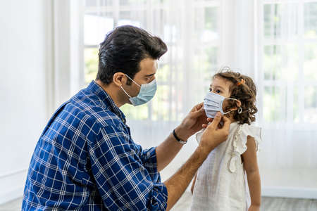 Father is wearing the face mask for little daughter, both are wearing face masks for confidence in their health.の写真素材