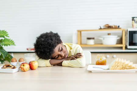 A little boy is sitting at the kitchen table leaning her face in her arms, concept for bullying, depression stress or frustrationの写真素材