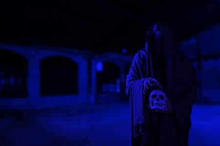 Horror scene of scary mysterious black man holding a skull in his hand at a creepy old building corridorの写真素材
