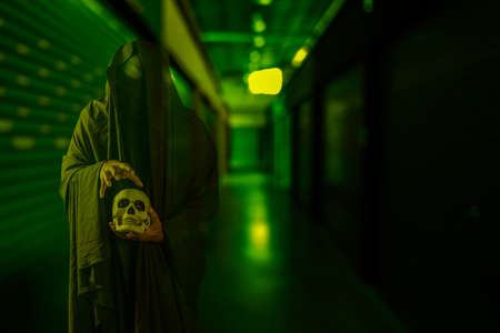 Horror scene of scary mysterious black man holding a skull in his hand at a creepy old building corridorの写真素材