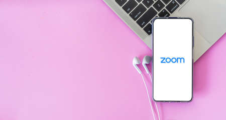 Bangkok, Thailand - September 6, 2021: Smartphone with earphones connected to Zoom video conference app logo on laptop keyboardのeditorial素材