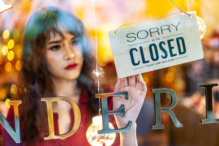 Young asian woman owner retail,coffee shop woman turning closed sign in door of store, protection to pandemic of virus.の写真素材