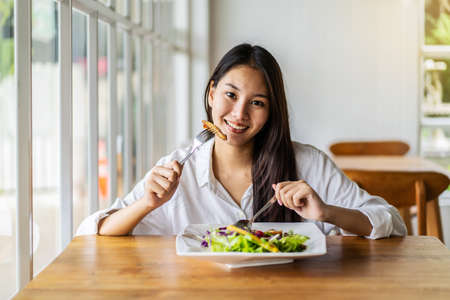 Portrait of attractive asian smiling young woman eating salad in restaurant, A young happy girl having a healthy lunchの写真素材