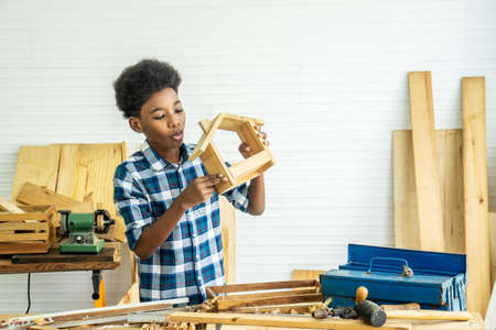 Smiling african american kid carpenter happy working with wood and sandpaperの写真素材