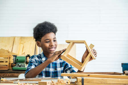 Smiling african american kid carpenter happy working with wood and sandpaperの写真素材
