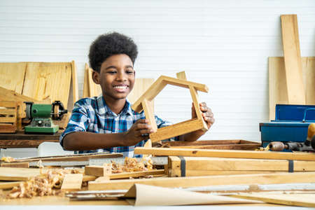 Smiling African-American boy carpenter looks at his own wooden house that helps his father happily do itの写真素材