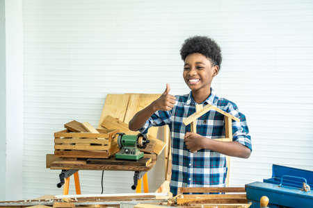 Smiling African-American boy carpenter looks at his own wooden house and thumbs up that helps his father happily do itの写真素材