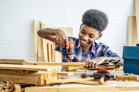Portrait of african american little child wearing shirt with a drill in hands and help dad assembling furniture shelf with power screwdriver tool, learning concept.の写真素材