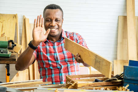 Young african american male carpenter sitting at table showing wooden items through tablet while video online chatting with customer or teaching online in factoryの写真素材
