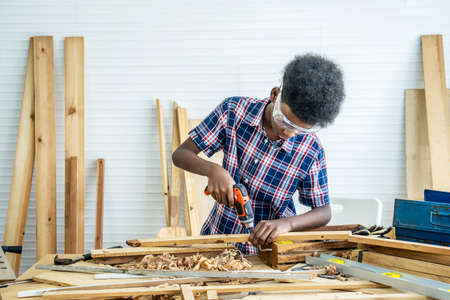 Portrait of african american little child wearing shirt standing with a drill in hands and help dad assembling furniture shelf with power screwdriver tool, learning concept.の写真素材