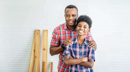 family, carpentry, woodwork, Portrait of cheerful african american father and little son standing by workplace in workshop, with diverse working tools laying on itの写真素材