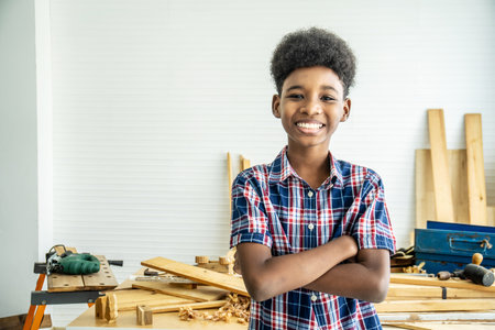 Smiling African-American boy carpenter standing with his arms crossed showing confidence After completing the woodwork that helped my father completeの写真素材