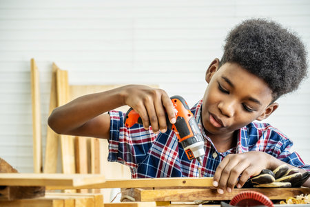 Portrait of african american little child wearing shirt with a drill in hands and help dad assembling furniture shelf with power screwdriver tool, learning concept.の写真素材