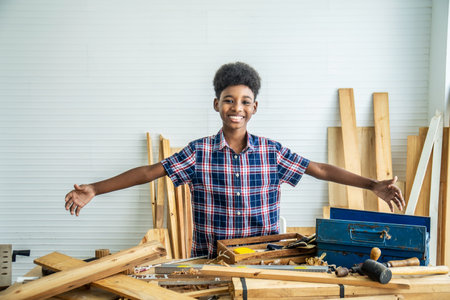 Smiling African-American boy carpenter spreading arms happily to show that the woodwork is placed on the table will try to succeedの写真素材