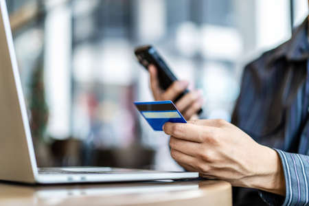 Businessman in casual shirt paying with credit card online while making orders via the Internet.Man's hands holding a credit card and using smart phone for online shopping. Selective focusの写真素材
