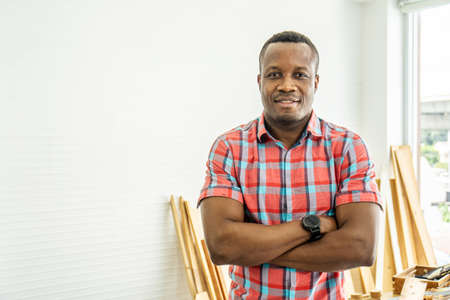 Portrait african american happy male woodworker or carpenter smiling, wearing shirt crossing arms for creating DIY wooden furniture as hobbyの写真素材