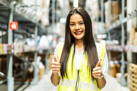 Portrait of smiling asian female staff in safety standing with showing thumbs up to look at the...