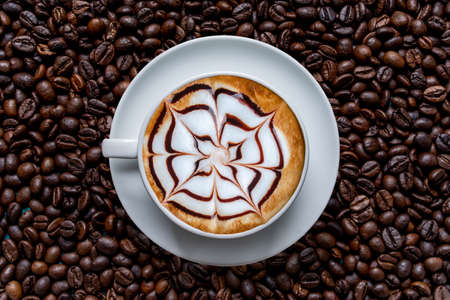 White cup of coffee frothy espresso stands on fresh roasted coffee bean background. Fragrant pleasure. Top view.の写真素材