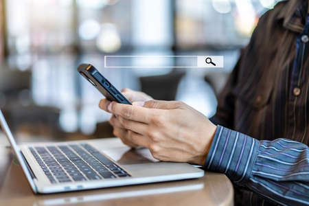 Data Search Technology Search Engine Optimization. Man hands using smartphones searching for information in internet online society web with search box icon and working via laptop on tableの写真素材