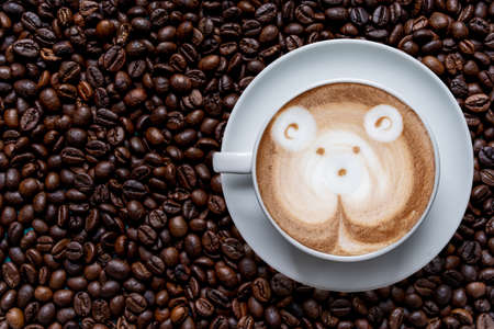 White cup of coffee frothy espresso stands on fresh roasted coffee bean background. Fragrant pleasure. Top view.の写真素材